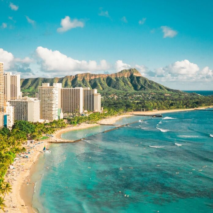a beach with buildings and a body of water with Diamond Head in the background