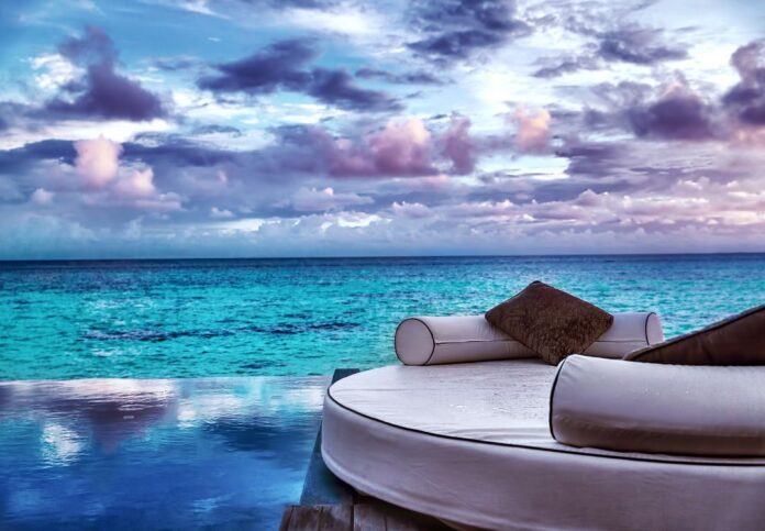 a round white bed with pillows on a deck overlooking a body of water