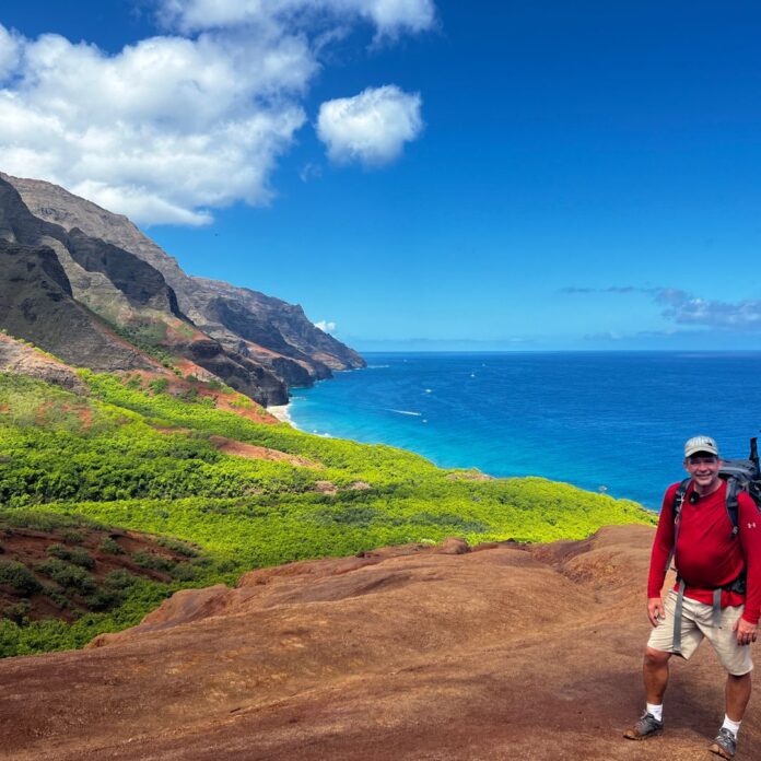 a man standing on a rocky cliff with a body of water in the background