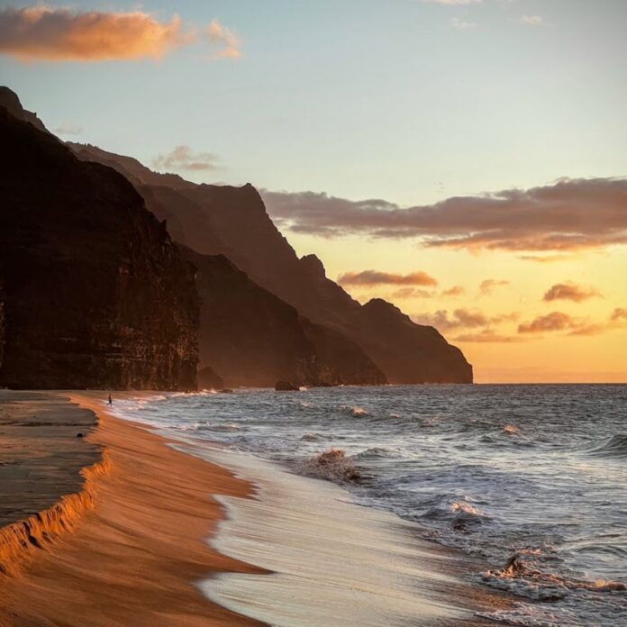 a beach with waves and mountains in the background