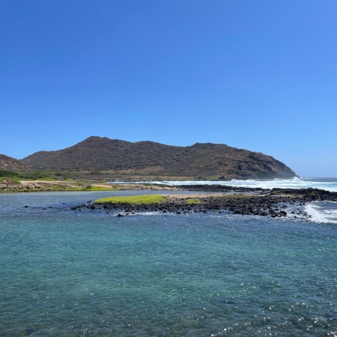 a body of water with a rocky island and hills in the background