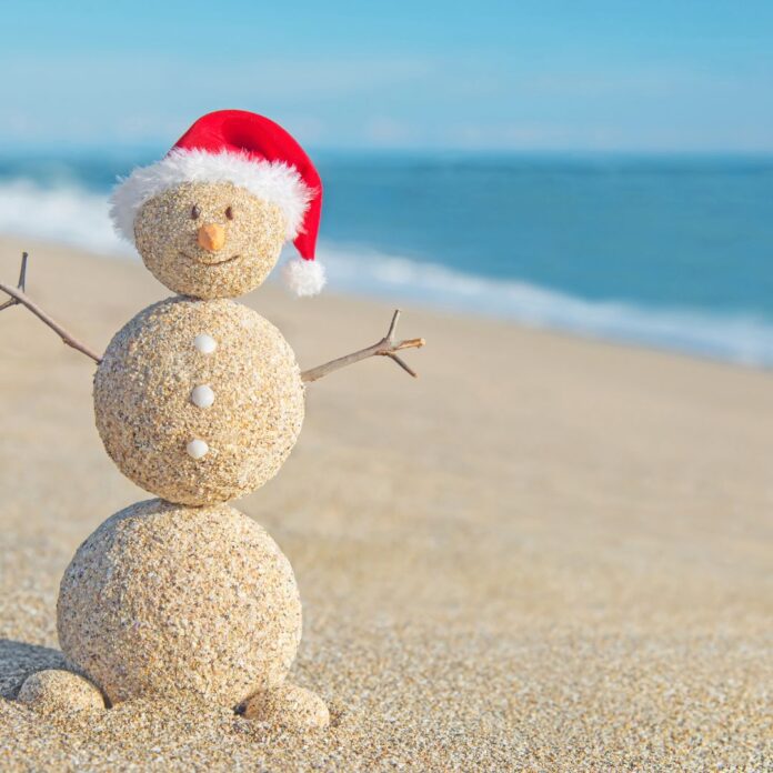 a snowman made of sand with a santa hat on the beach