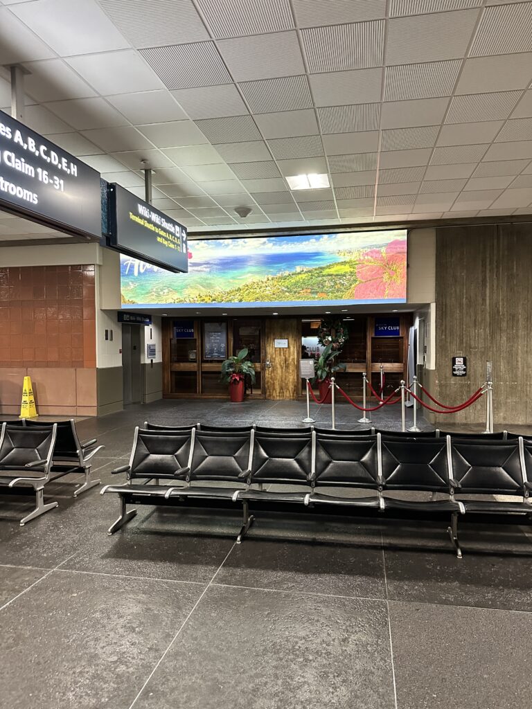 a row of chairs in a airport in front of the Delta Sky Club Honolulu