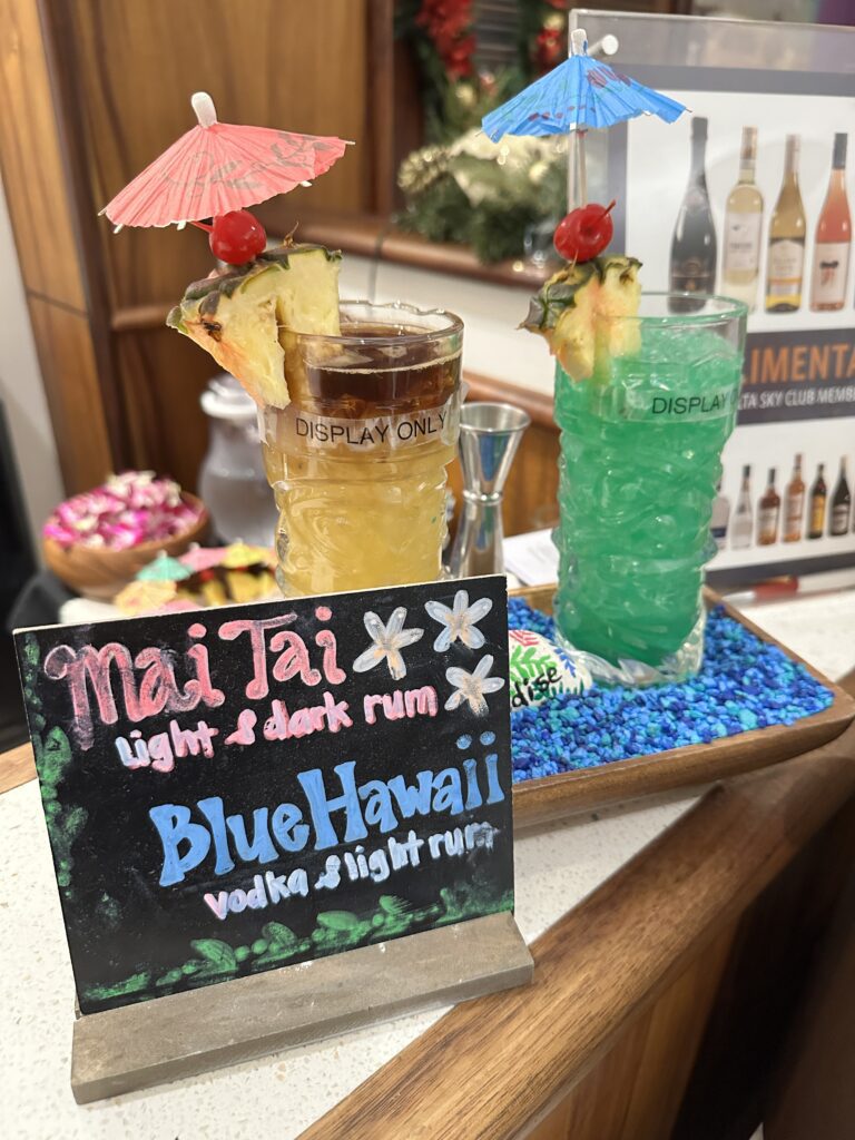 a drink with an umbrella and a sign on a tray at the Delta Sky Club Honolulu
